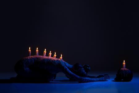 Burning candles on back of lady bowing down in darkness