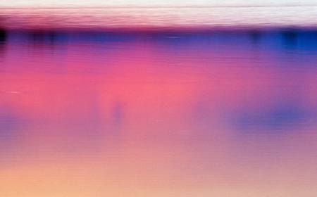 Farbenspiel von blau bis rosarot im Wasser durch einen Sonnenuntergang am See.